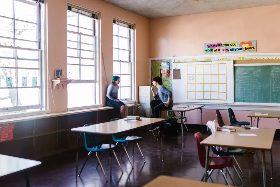 Zwei Erwachsene führen ein ruhiges Gespräch in einem leeren Klassenraum