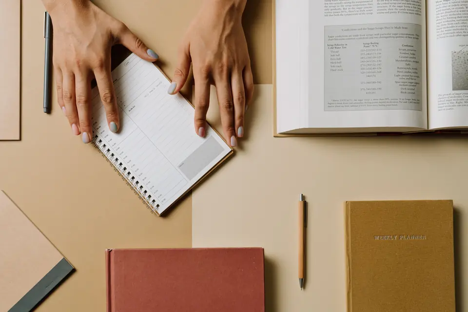Hände ordnen einen Wochenplan zwischen Büchern und Notizheften